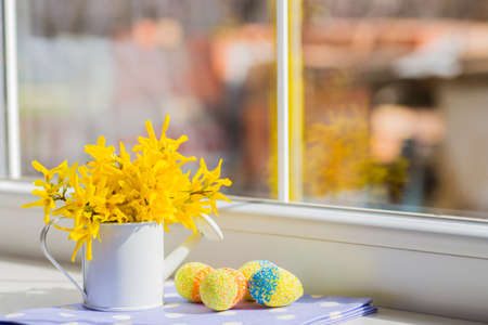 Colored easter egg and white little can with yellow flowers near window.の写真素材