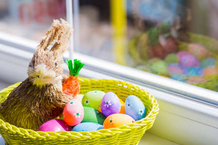 Wicker rabbit with colorful easter eggs in basket near window.の写真素材