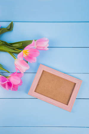 Bouquet of tender pink tulips with empty photo frame on blue wooden background.の写真素材
