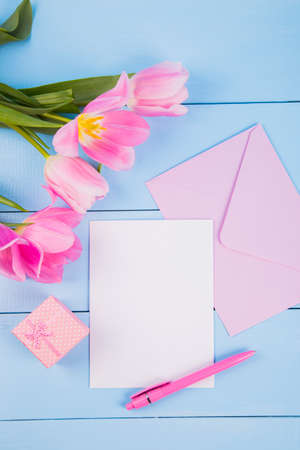 Bouquet of tender pink tulips with empty paper sheet, envelope and gift box on blue wooden backgroundの写真素材
