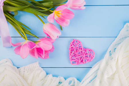 Bouquet of tender pink tulips with rattan heart and white fabric on blue wooden background.の写真素材