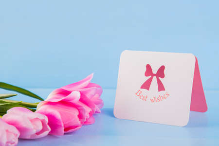Bouquet of tender pink tulips with greeting card on light blue wooden background.の写真素材