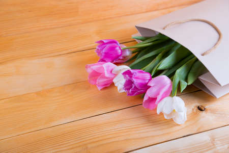 Beautiful bouquet of tender pink tulips in creamy shopping bag on wooden background.の写真素材