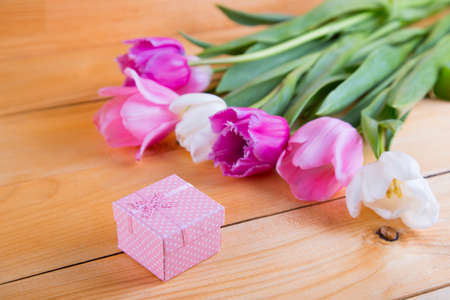 Bouquet of tender pink and white tulips with beautiful colored gift box on light wooden background.の写真素材