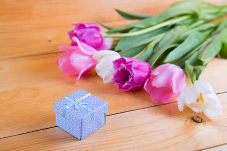 Bouquet of tender pink and white tulips with beautiful colored gift box on light wooden background.の写真素材