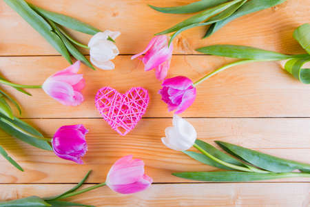 Beautiful bouquet of tender pink and white tulips with wicker rattan heart on light wooden backgroundの写真素材