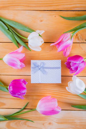 Beautiful bouquet of tender pink and white tulips with colorful gift box on light wooden backgroundの写真素材