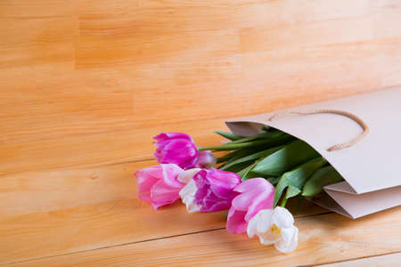 Beautiful bouquet of tender pink tulips in creamy shopping bag on wooden background.の写真素材