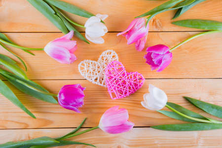 Beautiful bouquet of tender pink and white tulips with two wicker rattan hearts on light wooden backgroundの写真素材