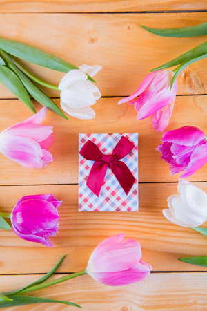 Beautiful bouquet of tender pink and white tulips with colorful gift box on light wooden backgroundの写真素材