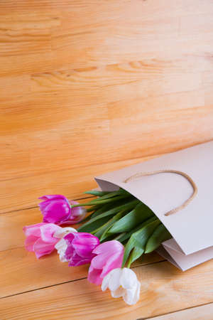 Beautiful bouquet of tender pink tulips in creamy shopping bag on wooden background.の写真素材