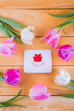 Beautiful bouquet of tender pink and white tulips with greeting card with inscription "Thank you" on light wooden backgroundの写真素材