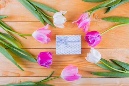 Beautiful bouquet of tender pink and white tulips with colorful gift box on light wooden backgroundの写真素材