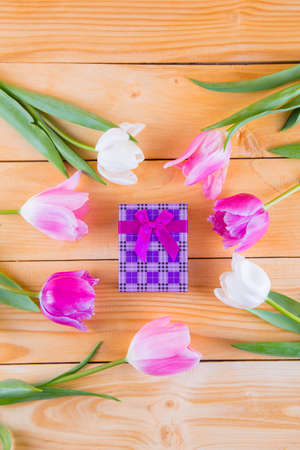 Beautiful bouquet of tender pink and white tulips with colorful gift box on light wooden backgroundの写真素材