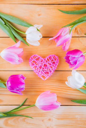 Beautiful bouquet of tender pink and white tulips with wicker rattan heart on light wooden backgroundの写真素材