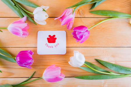 Beautiful bouquet of tender pink and white tulips with greeting card with inscription "Thank you" on light wooden backgroundの写真素材