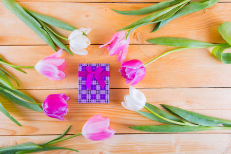 Beautiful bouquet of tender pink and white tulips with colorful gift box on light wooden backgroundの写真素材