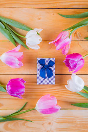 Beautiful bouquet of tender pink and white tulips with colorful gift box on light wooden backgroundの写真素材