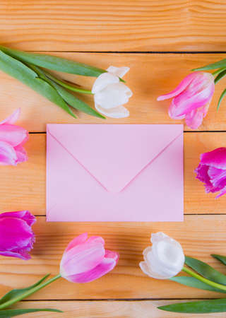 Beautiful bouquet of tender pink and white tulips with pink envelope on light wooden background.の写真素材