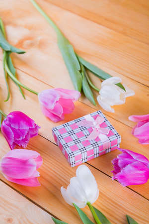 Beautiful bouquet of tender pink and white tulips with colorful gift box on light wooden backgroundの写真素材