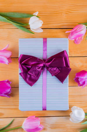 Beautiful bouquet of tender pink and white tulips with colorful gift box on light wooden backgroundの写真素材