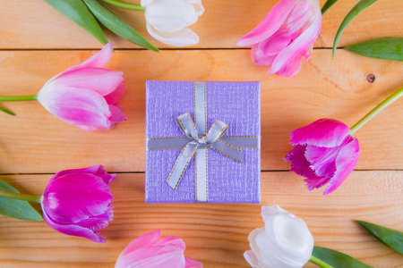 Beautiful bouquet of tender pink and white tulips with colorful gift box on light wooden backgroundの写真素材