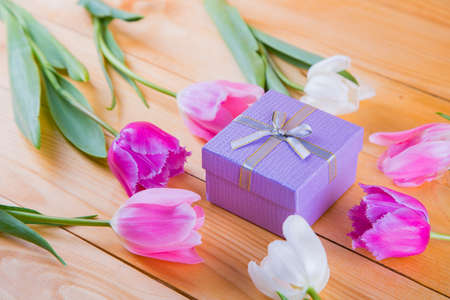 Beautiful bouquet of tender pink and white tulips with colorful gift box on light wooden backgroundの写真素材