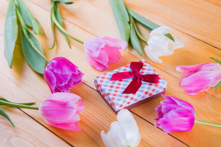 Beautiful bouquet of tender pink and white tulips with colorful gift box on light wooden backgroundの写真素材