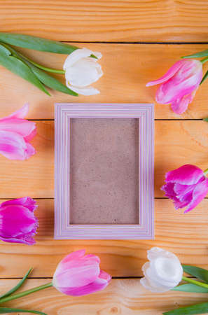 Bouquet of tender pink tulips with empty photo frame on light wooden background.の写真素材
