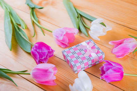 Beautiful bouquet of tender pink and white tulips with colorful gift box on light wooden backgroundの写真素材