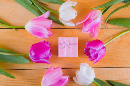Beautiful bouquet of tender pink and white tulips with colorful gift box on light wooden backgroundの写真素材