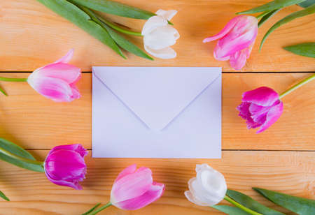Beautiful bouquet of tender pink and white tulips with white envelope on light wooden background.の写真素材