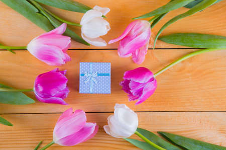 Beautiful bouquet of tender pink and white tulips with colorful gift box on light wooden backgroundの写真素材
