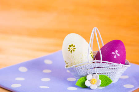 Two colorful yellow and crimson Easter eggs in white basket with white flower on spotted fabric on wooden backgroundの写真素材