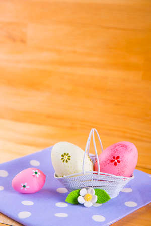 Colorful pink and yellow Easter eggs in white basket with white flower on spotted fabric on wooden backgroundの写真素材