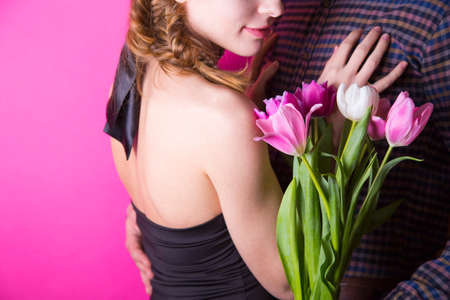 Beautiful young romantic couple with tender bouquet of pink and white tulips on bright crimson backgroundの写真素材