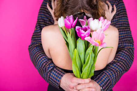 Beautiful young romantic couple with tender bouquet of pink and white tulips on bright crimson backgroundの写真素材