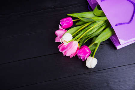 Beautiful bouquet of tender pink and white tulips in purple shopping bag on black wooden background. Spring romantic composition.の写真素材