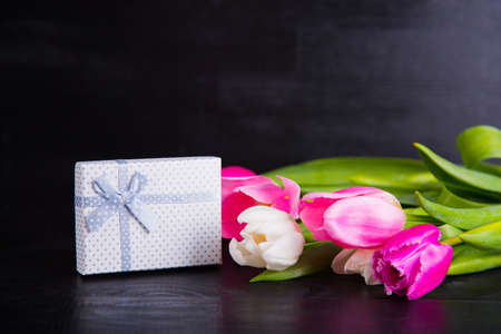 Beautiful bouquet of tender pink and white tulips and gift box on black wooden background. Spring romantic composition.の写真素材