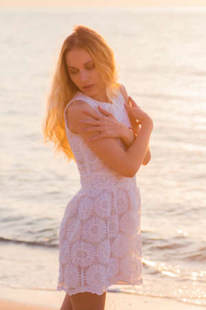 Beautiful young blond-haired girl on seaside at golden sunrise.の写真素材