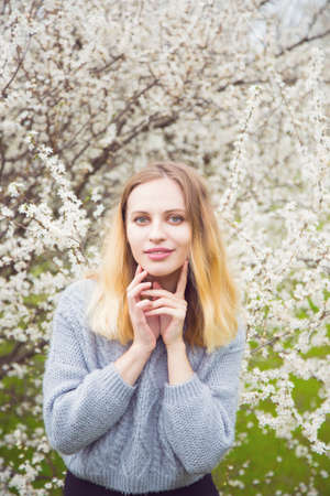 Beautiful blond young woman standing in front of wonderful blooming trees in spring garden. Vintage colors.の写真素材