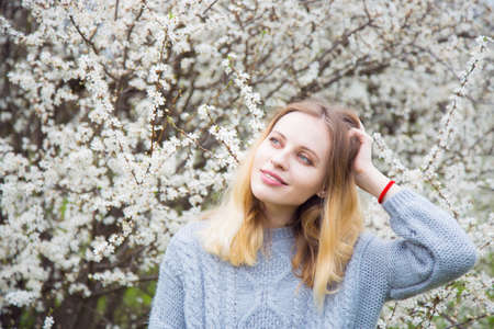 Beautiful blond young woman standing in front of wonderful blooming trees in spring garden. Vintage colors.の写真素材