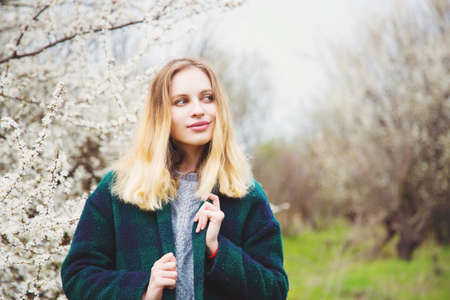 Beautiful blond young woman standing in front of wonderful blooming trees in spring garden. Vintage colors.の写真素材