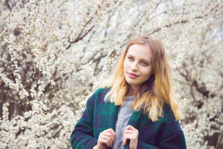 Beautiful blond young woman standing in front of wonderful blooming trees in spring garden. Vintage colors.の写真素材