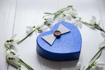 Beautiful tender white snowdrops with gift box in form of heart on white wooden background. Spring composition.の写真素材