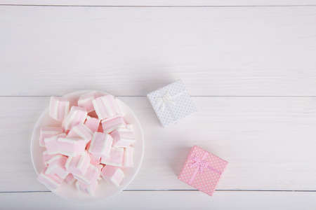 Soft pink and white marshmallow on plate with two gift boxes on white background. Pastel close-up sweets.の写真素材