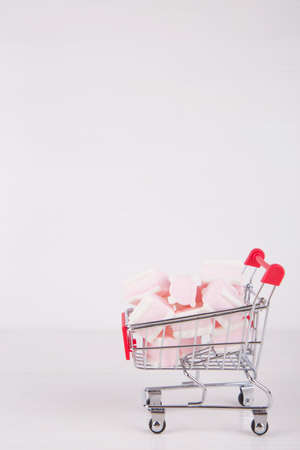 Small supermarket trolley with sweet pink and white marshmallow on white background. Pastel close-up sweets.の写真素材