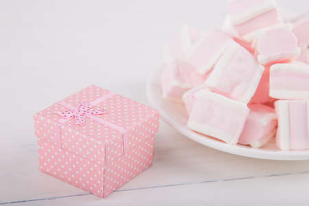 Soft pink and white marshmallow on plate with pink gift box on white background. Pastel close-up sweets.の写真素材