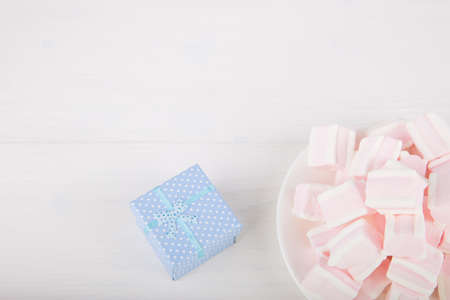 Soft pink and white marshmallow on plate with blue gift box on white background. Pastel close-up sweets.の写真素材