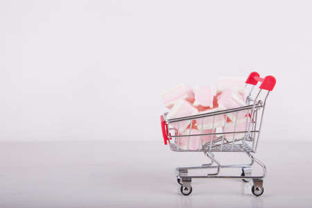Small supermarket trolley with sweet pink and white marshmallow on white background. Pastel close-up sweets.の写真素材
